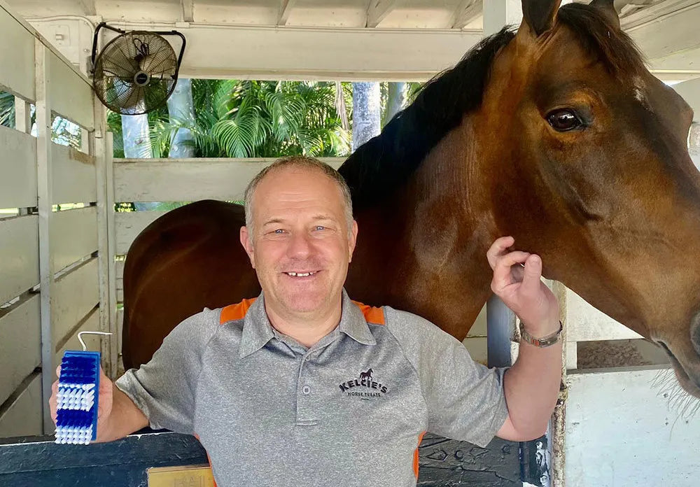 Man standing next to a horse in a stable with pickbrush