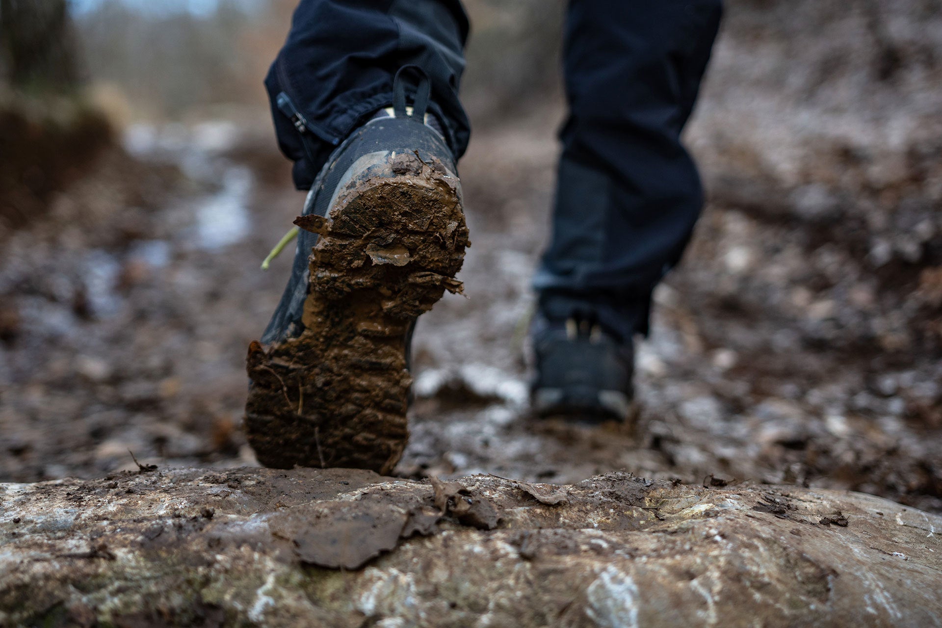 Person wearing muddy boots walking on a rocky path in a forest