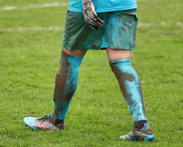 Person wearing muddy soccer cleats and shorts on a grass field