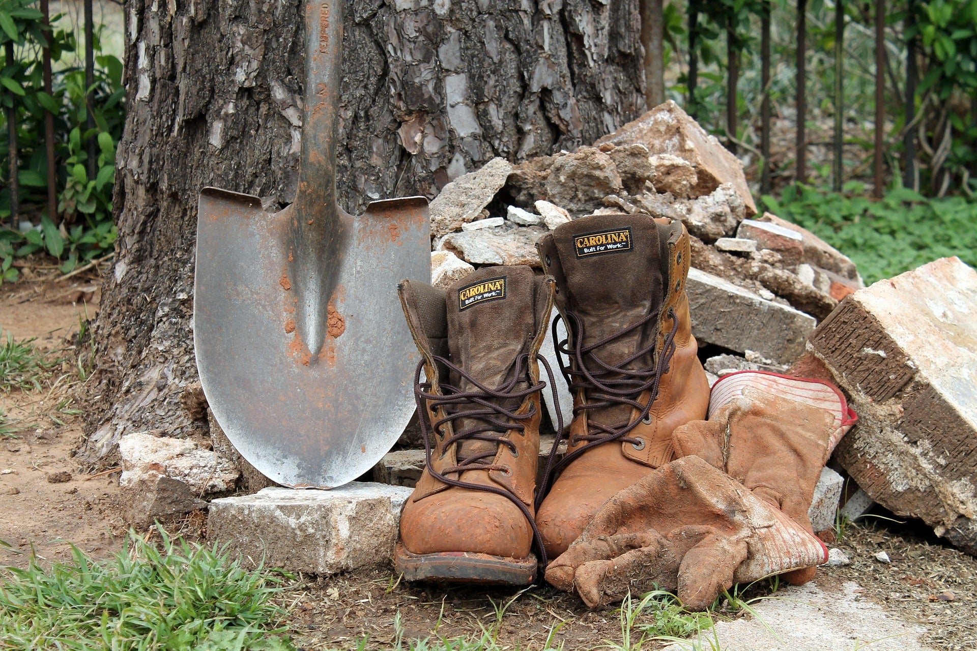 Brown work boots with a shovel leaning against a tree in an outdoor setting