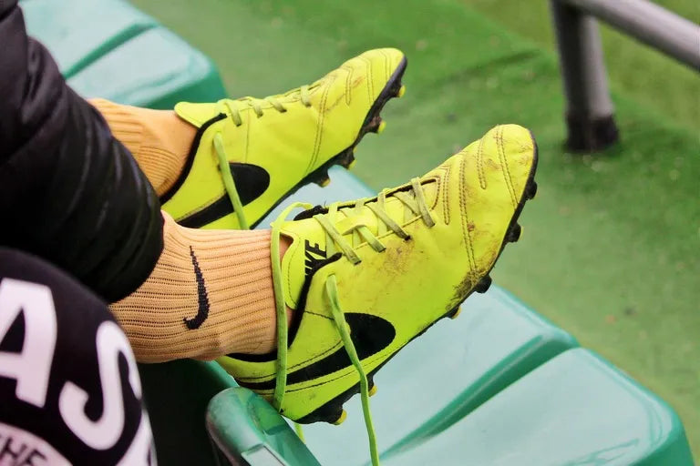Person wearing bright yellow soccer cleats with black Nike logo on a green bench.