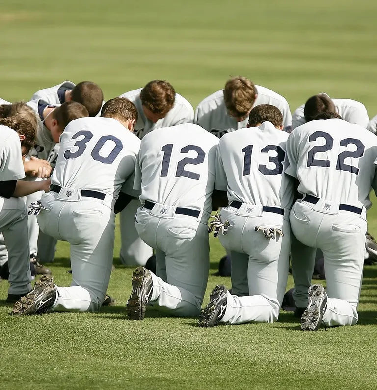Baseball players in white uniforms with numbers kneeling on a grass field